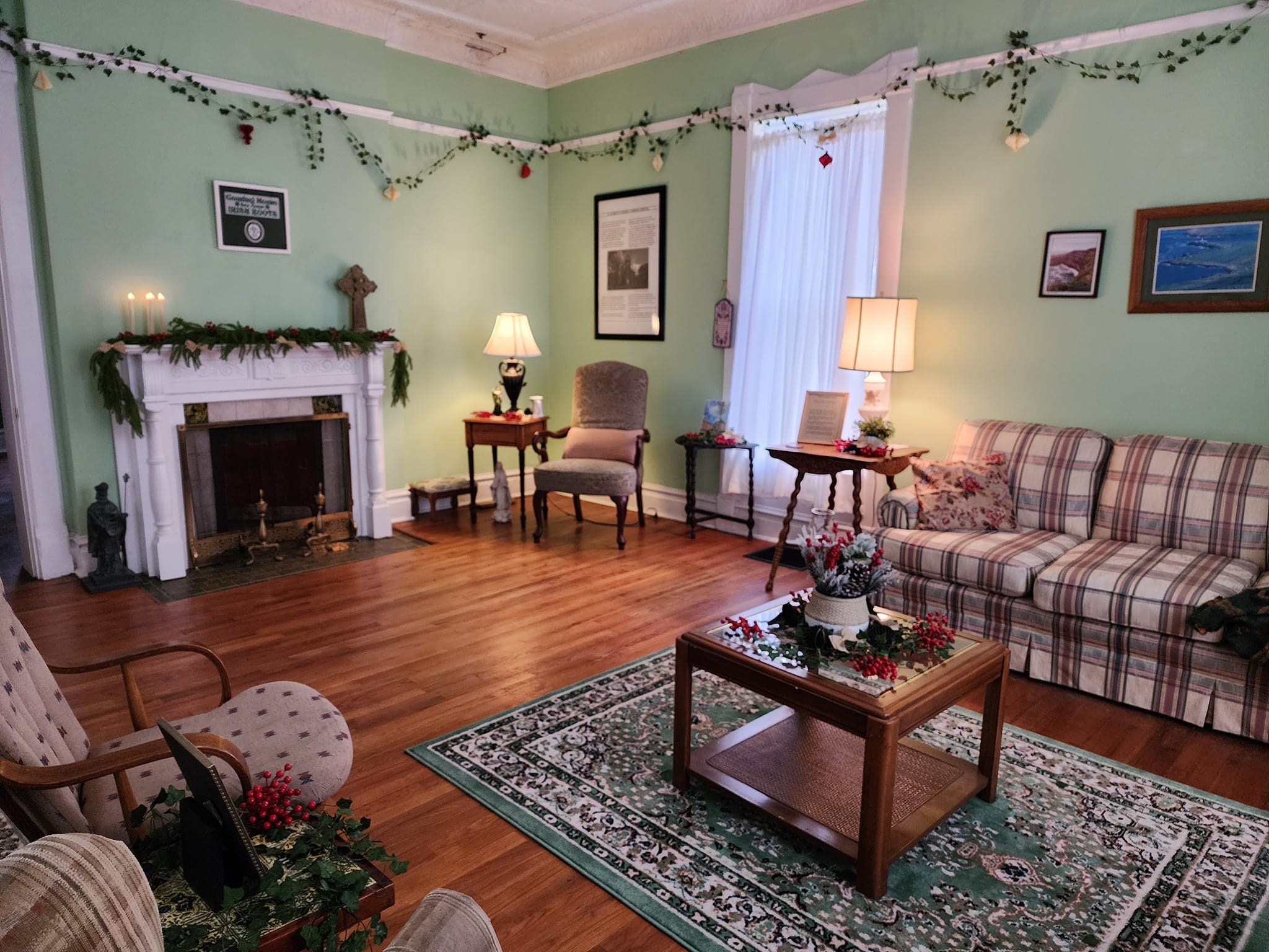The Hughes-Delaney room at Curran House decorated for Christmas with garland hanging from the map rails, the mantel decorated and a wreath on the coffee table